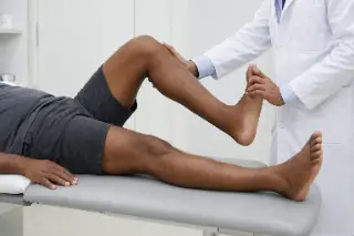 Physician Performing Leg Strength and Range of Motion Test - Clinical Stock Photo